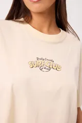 Remera coral cropped, de manga corta, con estampa trasera colorida de un perro surfeando y el texto "Rusty County Surf Club".