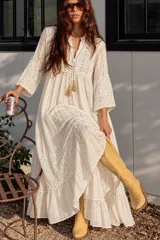 Vestido largo blanco de manga corta, confeccionado con tejido ligero y detalles de rayas brillantes doradas y paneles con bordados perforados. Cuenta con escote en V con cordones y borlas colgantes.