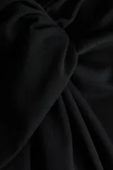 Pantalón de tiro alto negro, de corte holgado y pernera recta, confeccionado en punto grueso. Presenta un diseño drapeado con un detalle de nudo o giro en la parte frontal de la cintura.