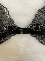 Conjunto de lencería compuesto por bralette triangular y tanga, confeccionado en encaje bitono negro y blanco. El bralette presenta cierre frontal con broche de gancho y breteles regulables. La tanga es de estilo colaless con laterales regulables mediante herrajes metálicos.