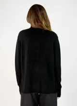 Sweater de punto gris con cuello alto, manga larga con puños acanalados y diseño holgado con costura central vertical.