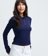 Blusa tipo polo de manga larga confeccionada en algodón, con cuello clásico y cierre frontal de botones. Presenta un diseño de corte regular y acabado suave.