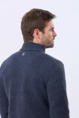 Buzo tejido de punto con textura en relieve, color azul marino. Presenta cuello alto con cierre frontal parcial y detalles en gamuza en la zona del cierre. Posee puños y ruedo acanalados.