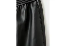 Pantalón negro de cuero sintético, de tiro medio con cintura elástica ajustable mediante cordón y diseño de pernera recta.