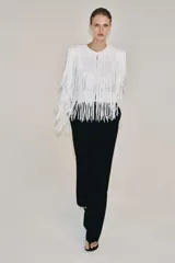 Chaqueta de cuello redondo y manga larga con hombreras, completamente cubierta de flecos con lentejuelas. Cuenta con forro interior y cierre frontal.