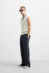 Chaleco de punto color crema con cuello en pico y ribete azul marino. Sin mangas y corte relajado.