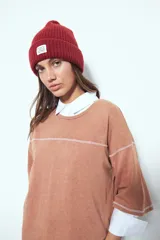 Remera de manga corta color marrón con efecto desgastado, corte oversize y costuras a la vista en color blanco. Presenta cuello redondo con cuello polo blanco superpuesto y mangas largas a rayas horizontales marrones y blancas por debajo.