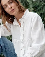 Camisa blanca de algodón con silueta holgada, detalles de tablas hechas a mano en el frente, cartera con botones y volados suaves en el cuello. Cuenta con mangas amplias y puños ajustables.