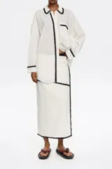 Falda pareo midi color blanco con bodoques negros a contraste y cierre con lazo en la cintura.