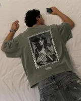 Remera oversize gris oscuro con corte holgado, mangas cortas y estampa trasera en blanco y negro con forma de estampilla que muestra a una persona con un gato y el texto 'Kaboa Industries'.