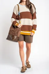 Sweater oversize de tejido de punto con diseño de rayas horizontales anchas en color beige y azul marino, cuello redondo marrón y puños y dobladillo en marrón con líneas beige y blancas.