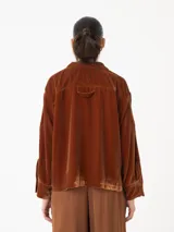 Camisa corta negra de terciopelo, de silueta cuadrada oversized, con bolsillo delantero y detalle en los puños y cuello con botón oro en forma de flor.