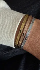 Set de tres pulseras rígidas tipo brazalete, con diseño de ondas grabadas. El set incluye una pulsera dorada, una en oro rosa y una plateada, todas fabricadas en acero.