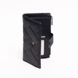 Billetera larga acolchada color negro, con diseño de costuras diagonales formando rombos. Cierre principal con broche a presión en solapa frontal. Presenta un pequeño tirador de cierre metálico en el borde superior izquierdo.