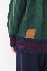 Buzo de tejido de punto con diseño de trenzas, color crema con detalles en marrón en cuello, puños y ruedo. Presenta líneas finas en contraste y pequeñas costuras decorativas en forma de cruz.