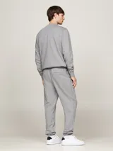 Pantalón de jogging gris de felpa de algodón, con cintura elástica ajustable con cordón, dos bolsillos laterales, un bolsillo trasero y bajos elásticos. Presenta el logo de Tommy Hilfiger bordado en el lateral.