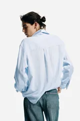 Camisa de manga larga en tejido liviano de mezcla de lino y viscosa, color celeste, con cuello clásico, cierre frontal de botones, bolsillo superior en el pecho y bajo redondeado.