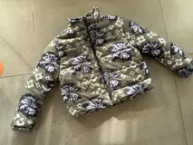Campera puffer color verde militar con estampado floral grande y detalles geométricos, cuello alto y cierre frontal con cremallera.