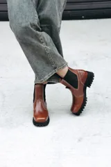 Bota tipo Chelsea de cuero color marrón, con paneles laterales elásticos en color negro y suela track robusta de goma negra.