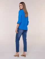 Blusa de calce relajado color salmón, confeccionada en tela liviana con textura sutil. Presenta escote en V con abotonadura frontal, bolsillo parche en el pecho, mangas largas regulables con presilla y ruedo con opción de anudar en el frente.