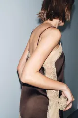 Top de tejido satinado color marrón oscuro, con escote recto y tirantes finos ajustables. Presenta aplicación de encaje color beige a contraste en el escote y el bajo.