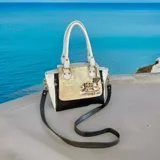 Cartera de cuero hecha a mano de la marca Carolina De Cunto, modelo Mila, con diseño tricolor en blanco, negro y detalle central dorado texturizado con arte pintado a mano. Cuenta con asas superiores blancas y herrajes metálicos.
