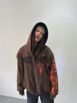 Campera reversible con cierre frontal. Un lado confeccionado en algodón color marrón con estampa plastisol en color naranja, bordados con apliques y capucha. El otro lado confeccionado en tela polar de pelo largo color negro con capucha.