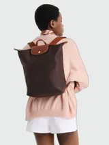 Mochila color marrón oscuro, modelo Le Pliage Original de Longchamp, con solapa y asas de cuero marrón y cierre de broche dorado.