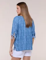 Blusa azul de lyocell con estampado floral, escote en V con bordado y aplique de cuentas de madera, mangas tres cuartos con lazos ajustables en los puños y diseño holgado.