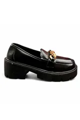 Mocasín de mujer color negro con acabado de charol, suela track robusta de plataforma y tacón cuadrado, con detalle de cadena dorada en el empeine.