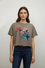 Remera de algodón color gris topo, con corte crop y ruedo sin costura. Presenta un estampado frontal de tres estrellas en tonos rojo, rosa y azul con efecto metalizado.