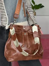 Bolso tipo bucket Chabas modelo Marin, confeccionado en cuero genuino de color marrón. Cuenta con diseño de cordón ajustable fruncido en la parte superior, manija corta decorativa de cuero con detalles metalizados y una correa larga intercambiable.