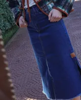 Pollera larga de denim azul de tiro medio, con diseño de corte evasé y terminación desmechada en el ruedo. Cuenta con abertura lateral y detalle de parche de cuero.