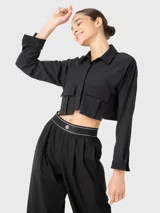 Blusa corta negra de manga larga con cuello camisero y dos bolsillos frontales con fuelle. Se puede usar abierta o cerrada. Combina con el pantalón Domi.