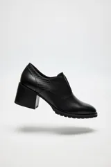 Zapato de cuero color beige, con taco de madera y suela dentada. Presenta un diseño slip-on con detalles de textura en relieve en los laterales y el empeine.