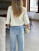 Chaqueta cropped de diseño estructurado en color crema, con cuello alto, cierre frontal cruzado con botones y mangas 3/4. Presenta un bolsillo decorativo en el frente y un corte asimétrico.