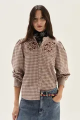 Camisa de manga larga con diseño de cuadros en tonos rosa y bordó. Presenta cuello mao, cierre frontal con botones y detalles de bordados florales en la parte superior del pecho. Las mangas son abullonadas con puños ajustados.