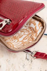 Bandolera porta celular color rojo con textura croco, cierre de cremallera plateada y correa fina ajustable.