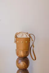 Cartera tipo canasta color marrón claro, con tachas doradas y correa larga ajustable.