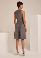 Bermuda gris de tejido plano con diseño entallado, cinturilla con trabillas y cordón, pinzas delanteras, bolsillos delanteros y traseros, cierre frontal y dobladillo en el ruedo.