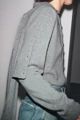 Chaqueta de tejido de punto color verde musgo, de corte cropped, con cuello redondo y cierre frontal de botones oscuros.