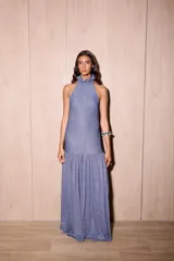 Vestido largo azul con acabado brillante, corte holgado, escote halter con cuello alto con volado y falda con maxi volado a la altura de la cadera.