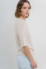 Buzo de tejido abierto color beige claro, de calce oversize con mangas 3/4 y cuello redondo. Presenta terminaciones acanaladas en puños y cintura.