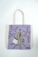 Bolso tipo tote bag de color crudo con estampado de flores celestes y centros azul oscuro. Cuenta con doble asa de hombro en tono crudo y etiqueta con la marca en el frente.