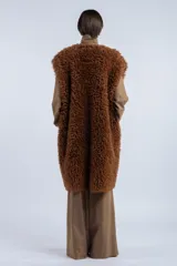 Chaleco largo reversible de diseño versátil. Por un lado, presenta una textura de peluche sintético en color marrón, y por el otro, un acabado liso. Cuenta con cierre frontal de botones y corte recto.