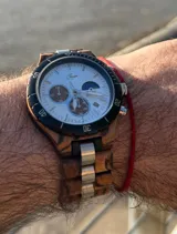 Reloj cronógrafo con caja de madera de zebrano y bisel técnico de acero negro. La esfera es plateada con subdiales de madera, indicador de fase lunar y fechador. La malla combina eslabones de acero inoxidable con madera de zebrano.