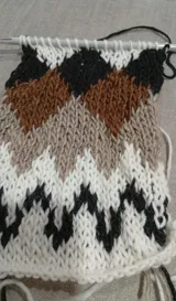 Sweater de punto tejido a mano, con diseño de grecas nórdicas en tonos blanco, marrón y negro en la parte superior. Presenta cuello redondo y mangas largas, con una textura suave y abrigada.