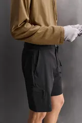 Bermuda negra de ajuste regular, confeccionada en tejido técnico compacto con elasticidad. Presenta cintura ajustable con cinturón a contraste, bolsillos frontales y un bolsillo cargo con cierre de cremallera oculta en la pernera.