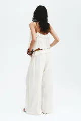 Pantalón oversized de tiro bajo color blanco crudo, confeccionado en viscosa con alforzas, ribetes de encaje, cordón de ajuste y ribete de volado en la cintura.