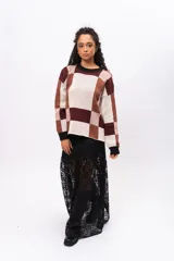 Buzo de tejido de punto con diseño geométrico de cuadros en tonos marrones, beige y bordó. Presenta cuello redondo, puños y borde inferior en color negro, con mangas largas y corte holgado.